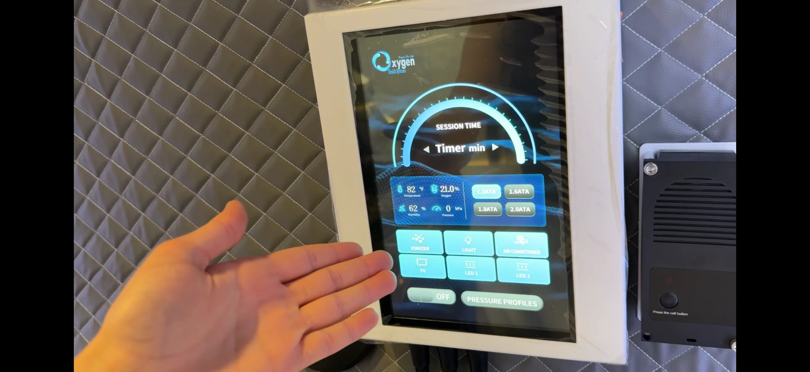 Intuitive high-definition internal touchscreen user interface mounted inside the chamber — showing session timer, real-time temperature, oxygen, humidity and pressure readouts, one-touch ATA pressure selection, and chamber controls