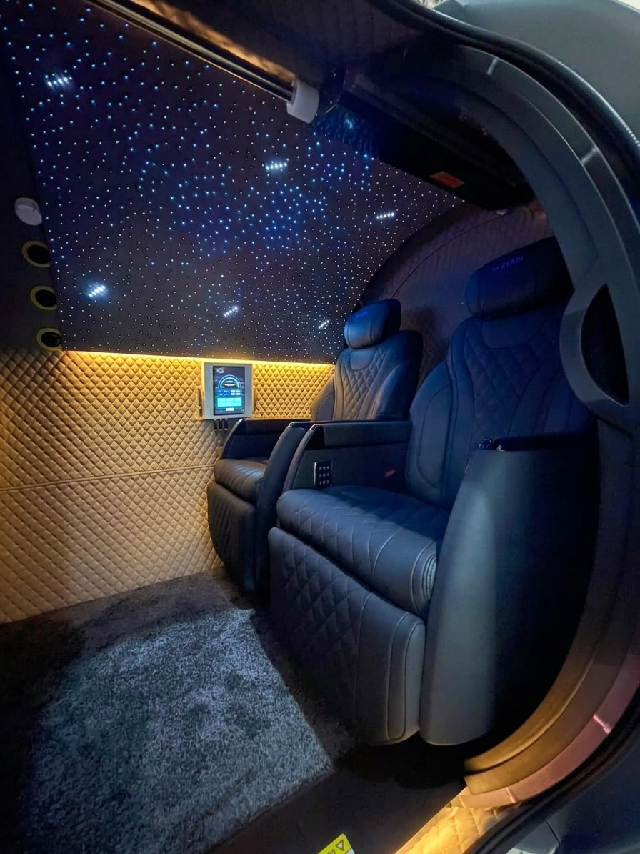 Two navy quilted-leather reclining captain's chairs inside the M5502 cabin beneath a fiber-optic starlight ceiling, with gold quilted padded wall lining, ambient under-lighting, a mounted touchscreen, and plush gray carpet